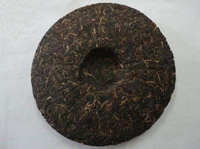 Compressed pu-erh tea cake with dark, textured surface on white background