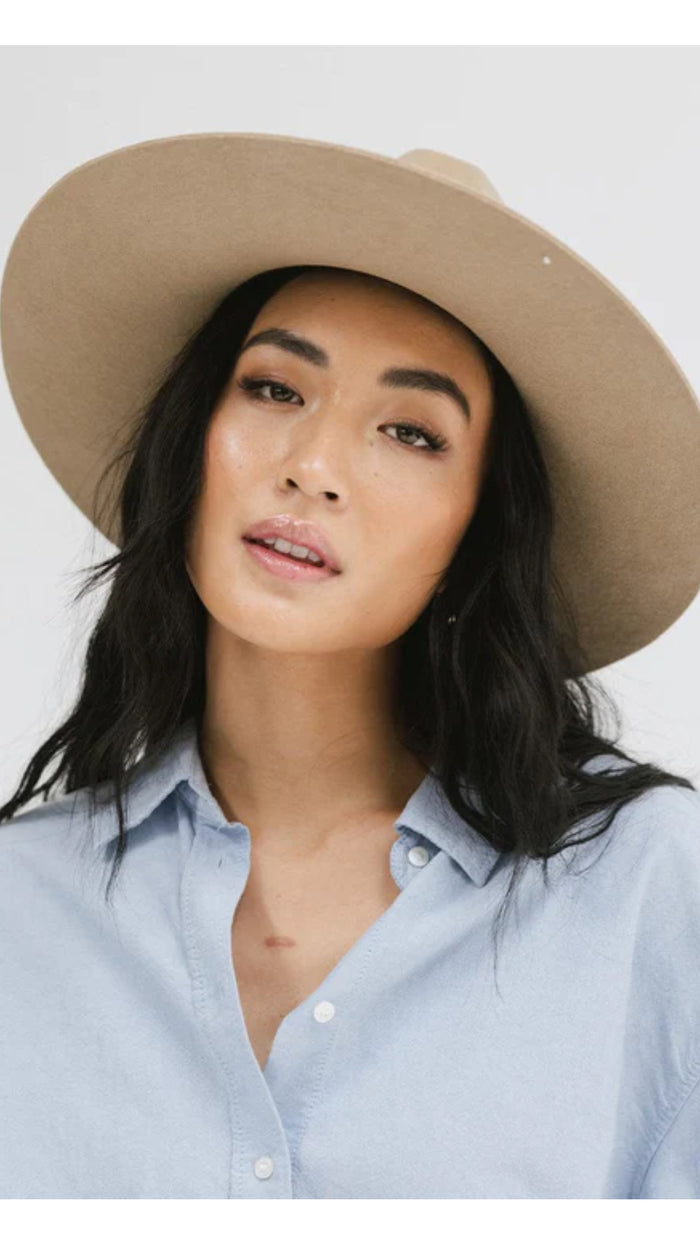 Woman wearing a beige wide-brimmed hat and light blue button-up shirt, showcasing feminine classic style