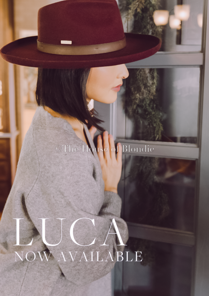Woman wearing burgundy wide-brim hat and gray sweater, indoor cozy boutique setting, elegance