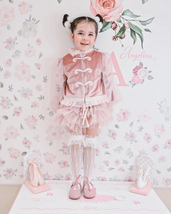 Clara Pink Velour Jacket and Bloomers Set styled on toddler with lace knee socks and Mary Jane shoes against soft pink floral wallpaper.