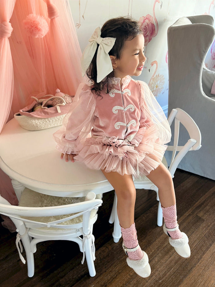 Toddler modeling Clara Pink Velour Jacket and Bloomers Set with pink headband, sheer sleeves, and ruffled waist detail.
