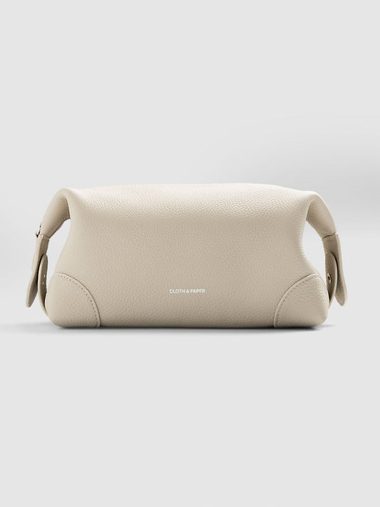 Folded Form Pouch in warm beige pebbled leather, three-quarter view, snapped closed with silver foil Cloth & Paper logo visible on exterior