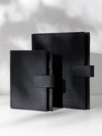 Two black leather agendas displayed against a shadowed background.