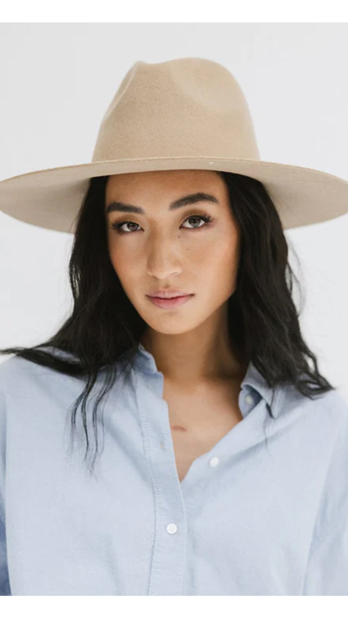 Stylish woman wearing a beige wide-brimmed hat and light blue button-up shirt in studio