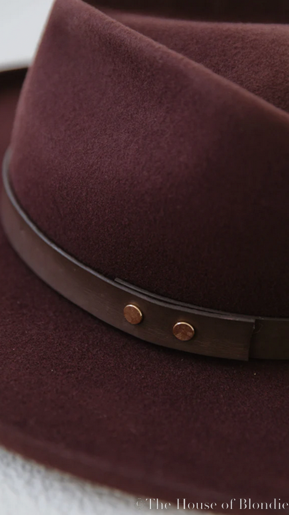 Close-up of dark cherry felt women's fedora with brown leather band and copper studs from The House of Blondie