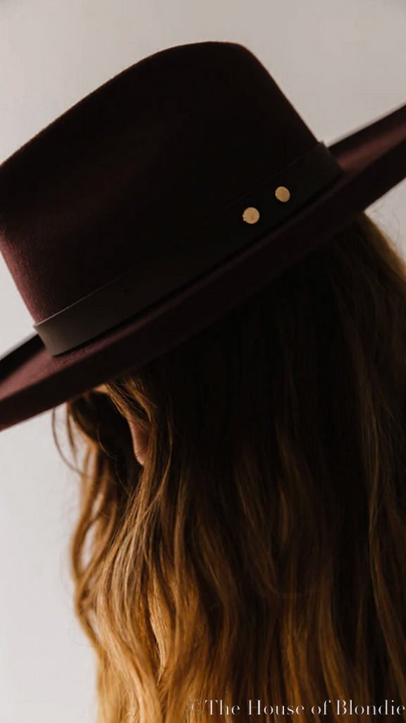 Dark cherry wide-brim hat with black band and gold studs on woman with wavy hair