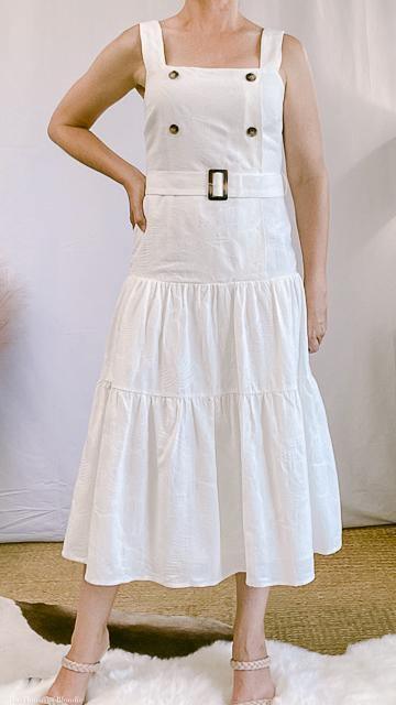 Elegant white sleeveless belted midi dress with square neckline and tiered skirt, styled for upscale women's boutique