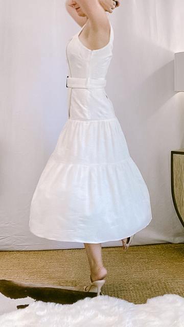 Woman wearing a sleeveless white belted midi dress spinning in a minimalist room with neutral decor
