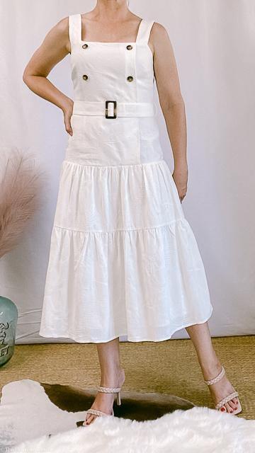 Woman wearing a sleeveless white belted midi dress with button details in an upscale women's boutique setting