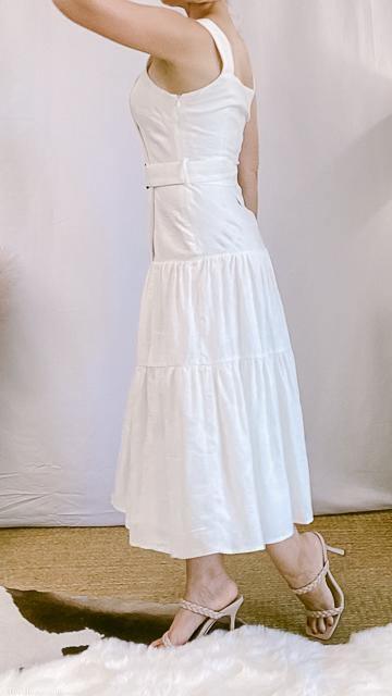 woman wearing sleeveless white belted midi dress with tiered skirt and strappy heels in boutique setting