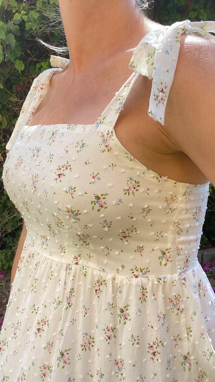 Close-up of a woman wearing a white floral self-tie strap midi dress with textured fabric outdoors
