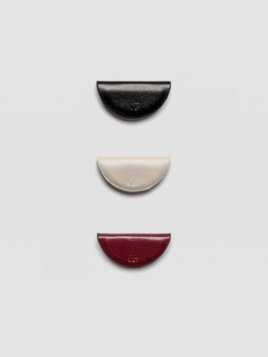 A set of three semi-circle leather magnetic bookmarks in black, cream, and burgundy colors