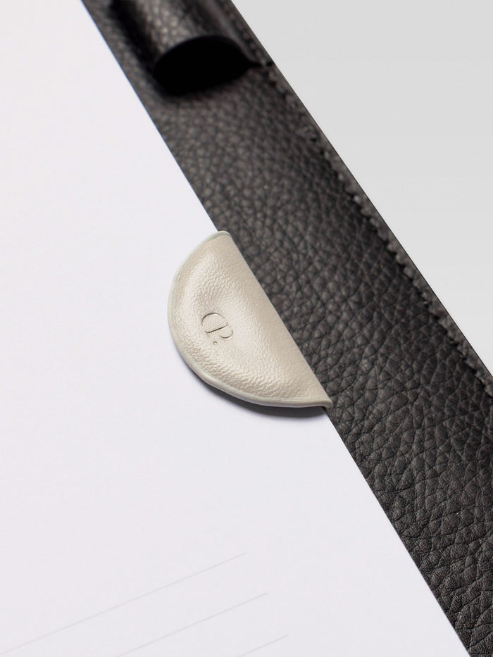 Close-up of the cream leather magnetic bookmark clipped onto a planner page with a black leather cover.