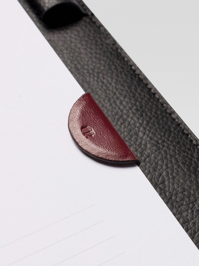 Close-up of the burgundy leather magnetic bookmark attached to a planner page with a black leather cover.