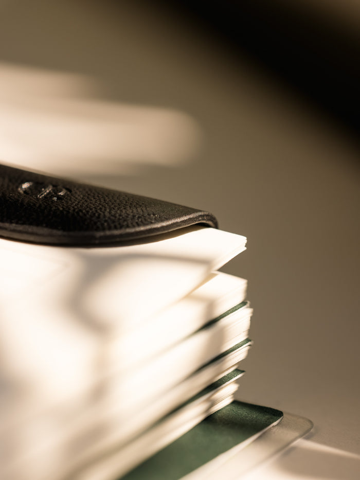 A black Mini eCLIPse bookmark clipped onto the pages of a stacked planner, highlighting its sleek design and low profile.