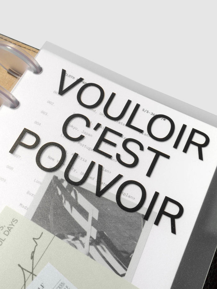 Close up image of the top right corner of the Moments Cover and Dashboard displayed in black folio with clear discs.  The text reads Vouloir C'est Pouvoir. It is turned at a slight angle on a neutral background.