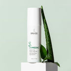 A bottle of ORMEDIC® balancing facial cleanser | IMAGE Skincare positioned next to fresh green aloe vera and leaves on a pale green background, emphasizing natural skincare and wellness.