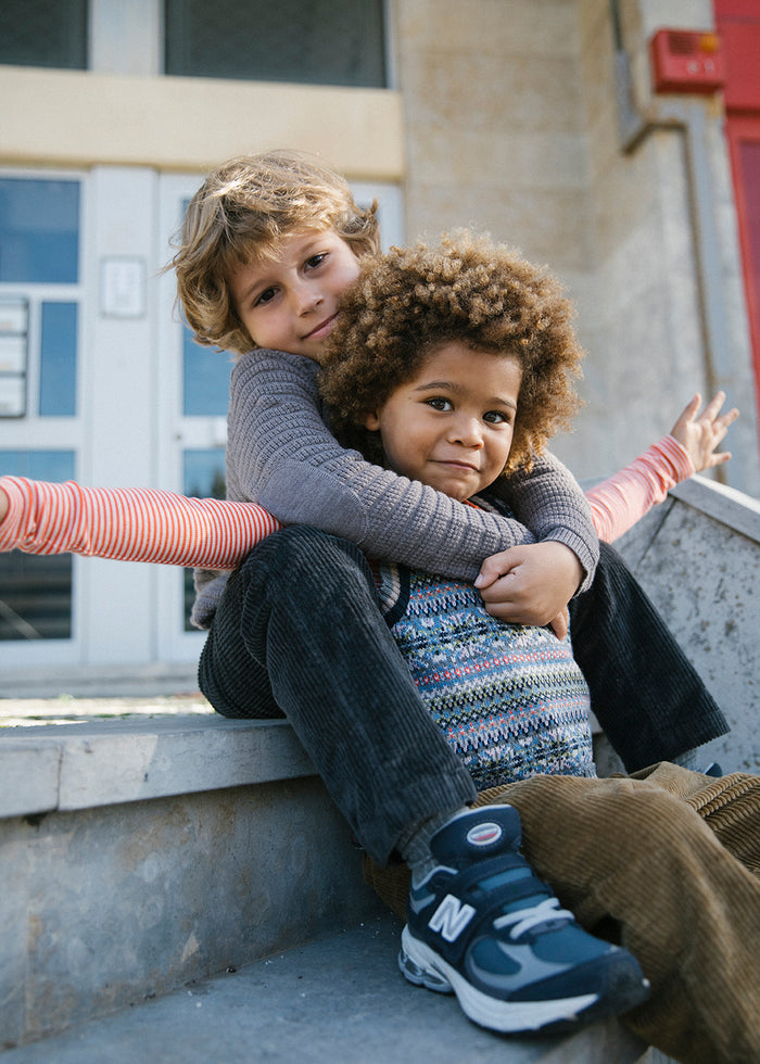 Two children sitting together, one in a patterned knitted vest
