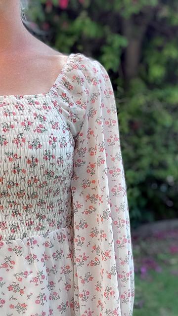 Close-up of a white Tallulah square neck midi dress with ditsy pink floral print and smocked bodice, outdoors