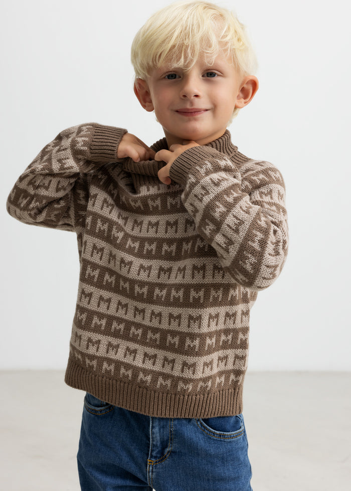 Child puts on a brown M-patterned sweater, smiling