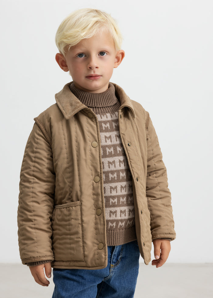 Child wearing brown knitted sweater with M pattern and quilted jacket over it