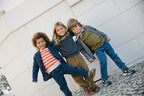 Three children wearing knitted cardigans and jeans playing outdoors