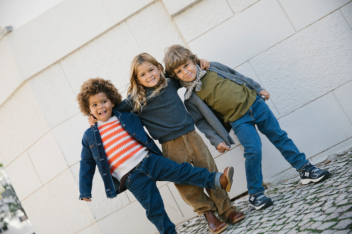 Three children wearing knitted cardigans and jeans playing outdoors