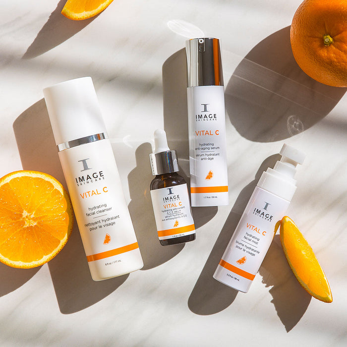 VITAL C hydrating anti-aging serum | IMAGE Skincare displayed with other skincare products and fresh orange slices, highlighting brightening and hydrating benefits.