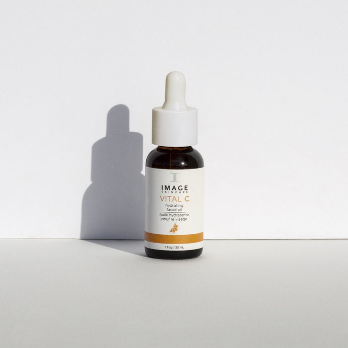 Bottle of VITAL C hydrating facial oil | IMAGE Skincare with a white dropper cap casting a shadow on a white surface and neutral background.