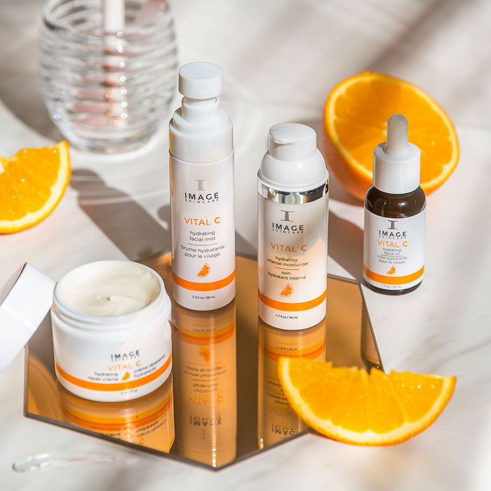 Set of VITAL C hydrating facial oil | IMAGE Skincare products displayed on a mirrored surface with fresh orange slices, promoting skincare and hydration.