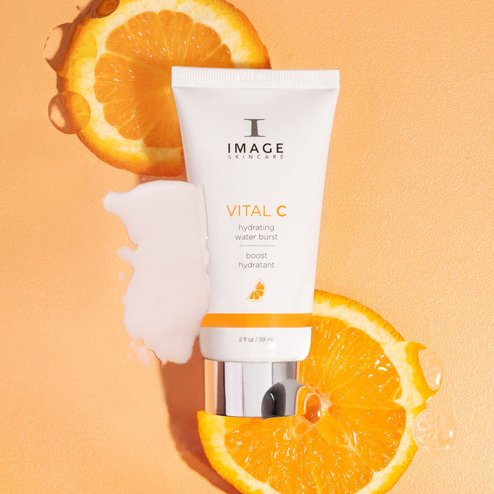 VITAL C hydrating water burst | IMAGE Skincare tube placed on orange background with sliced fresh oranges and a splash of hydrating serum for skincare and wellness.